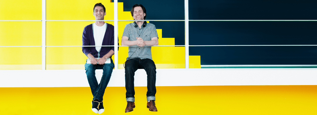 Due uomini sorridenti su uno sfondo giallo in un ufficio